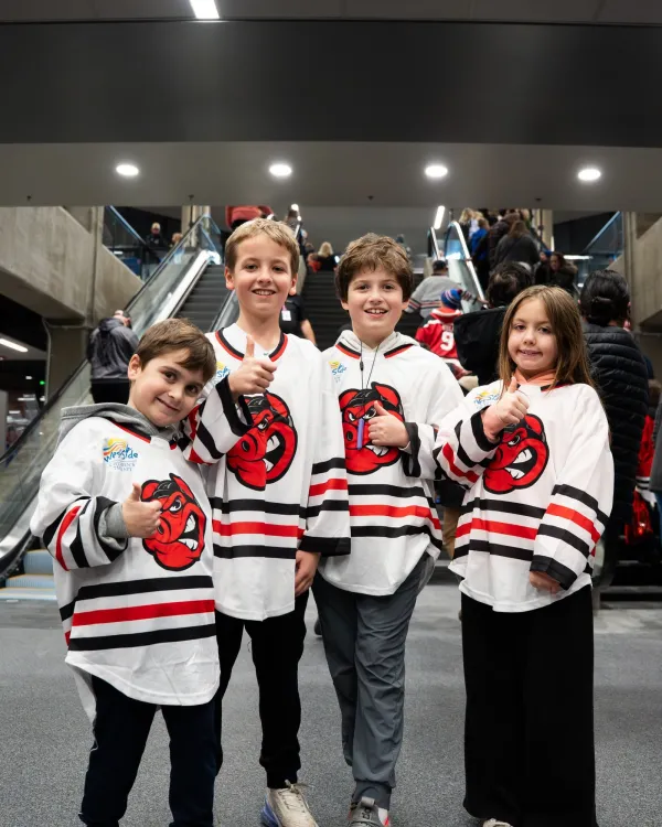 Four kids at IceHogs youth jersey night pose in their white jerseys while giving a thumbs up